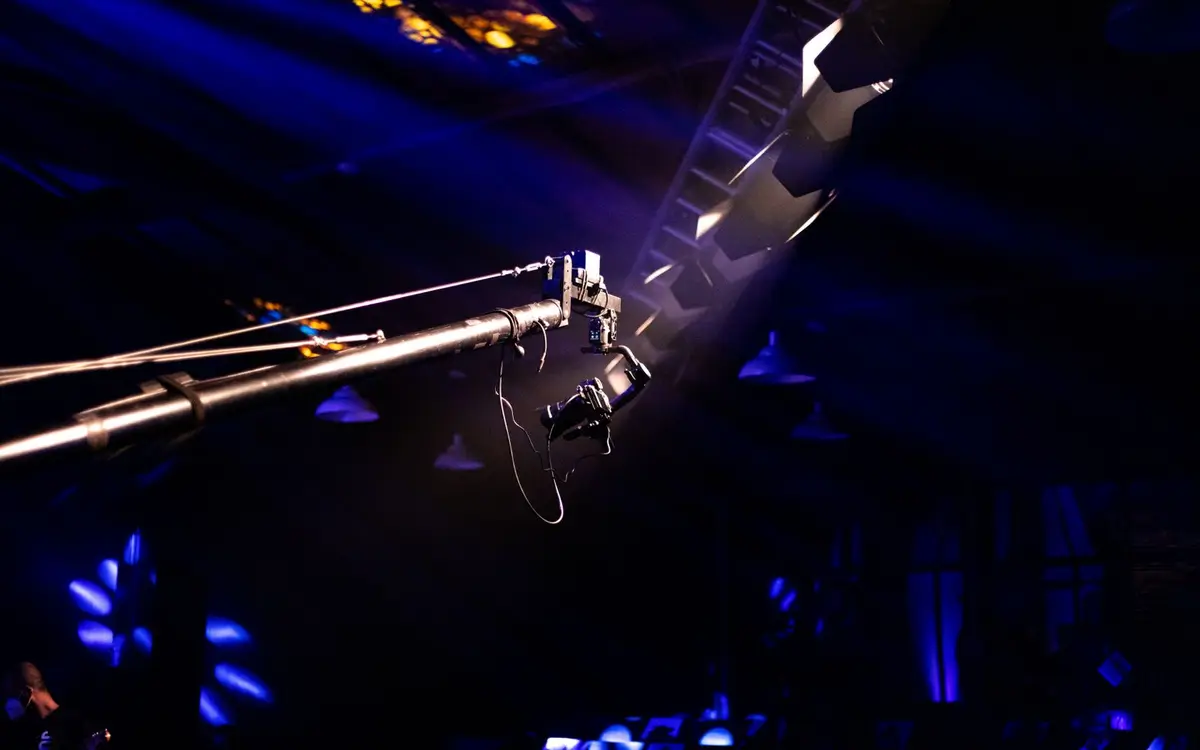 A camera crane arm over a production floor under blue and violet lighting