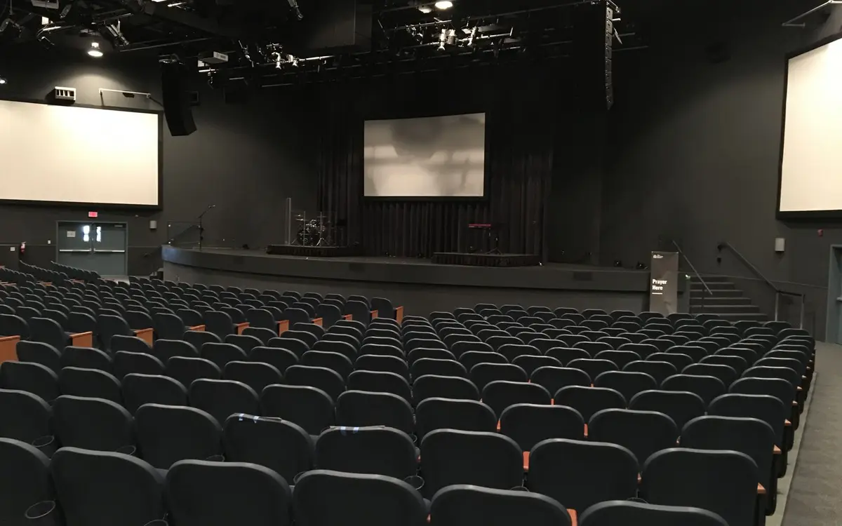An empty conference auditorium with tiered seating facing a stage and two projection screens