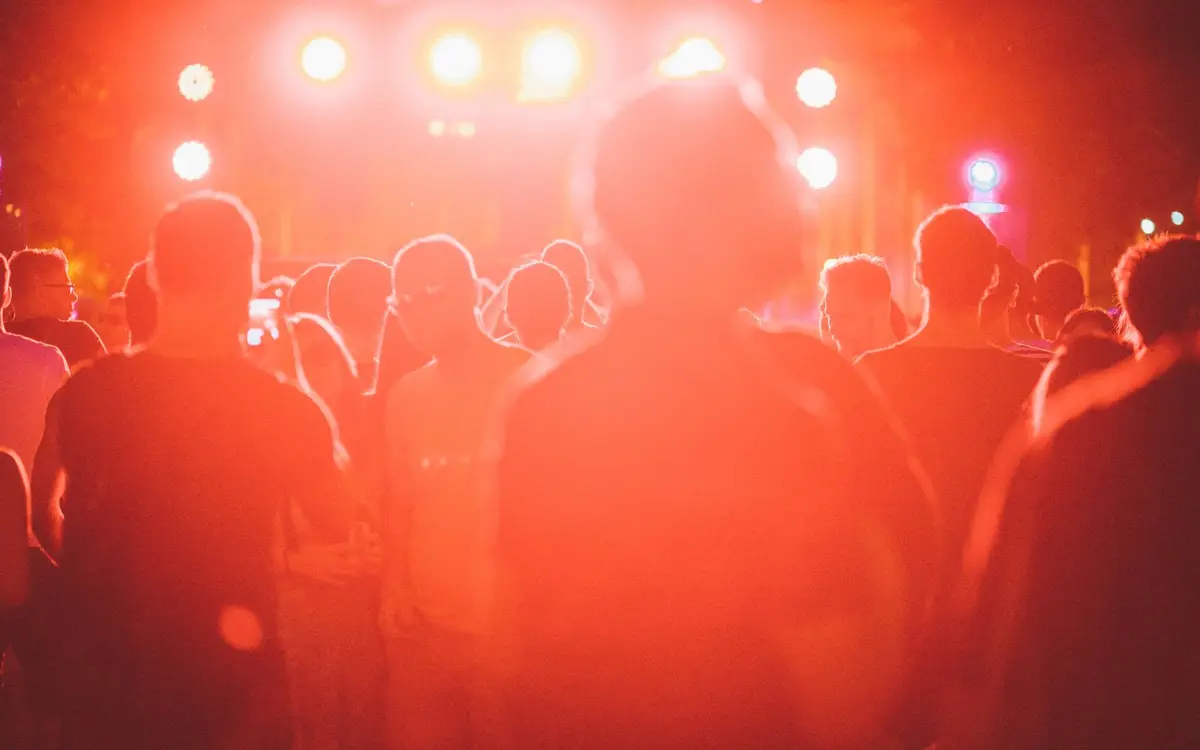 A festival crowd seen from behind, backlit by red stage lights