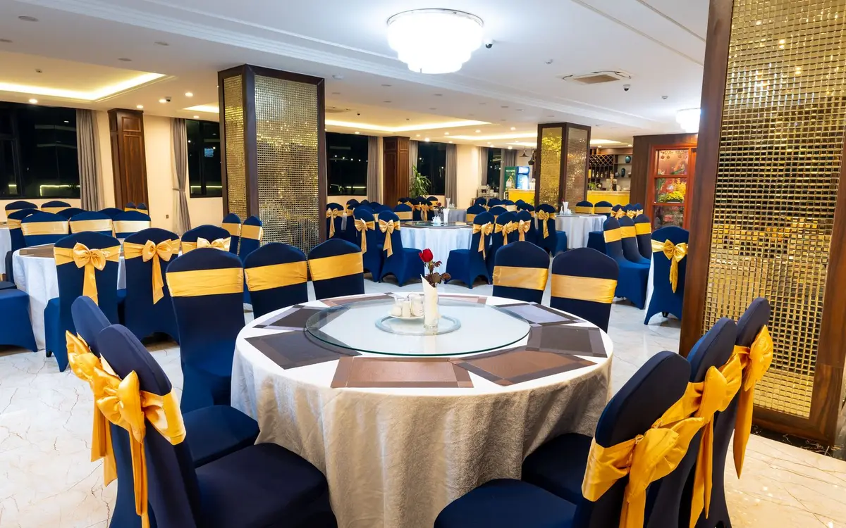 A banquet hall set for a formal dinner, round tables dressed with gold sashes on navy chairs