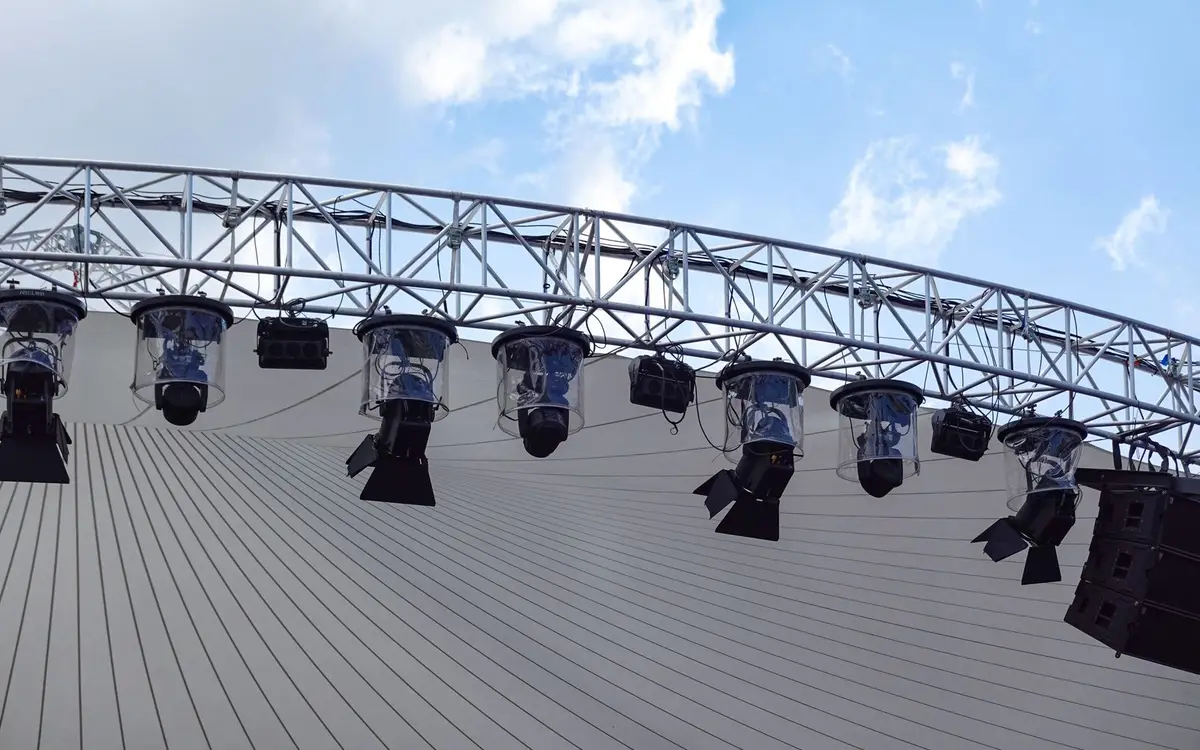 Stage lighting fixtures hanging from an outdoor truss against a blue sky