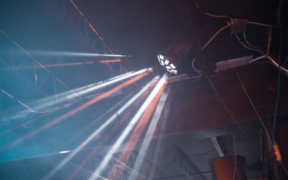 Beams from a moving-head stage light crossing an industrial ceiling